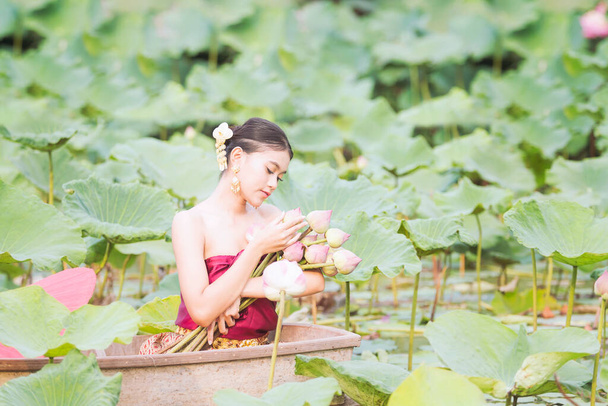 Women wearing Thai dresses are admiring lotus flowers. Asian women sitting on wooden boats to collect lotus. Beautiful girl wearing traditional Thai dress hand holding a flowers. - Photo, Image