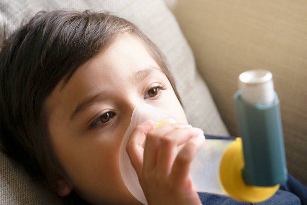 Φτωχό αγόρι έχουν ένα πρόβλημα με το βήχα στο στήθος κρατώντας μάσκα εισπνοών, Παιδί χρησιμοποιώντας το volumtic για την αναπνοή θεραπεία, Παιδί που έχει αλλεργία στο άσθμα χρησιμοποιώντας το άσθμα εισπνευστήρα, Υγεία και ιατρική έννοια - Φωτογραφία, εικόνα