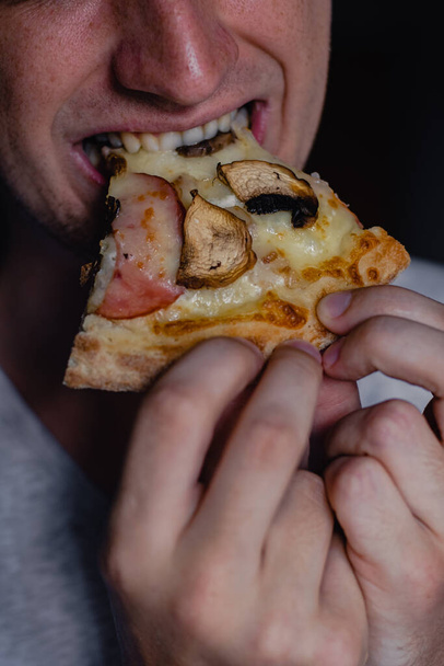 Close up retrato de animado jovem faminto feliz comendo um pedaço de pizza, foco de pizza. Jovem caucasiano homem comendo pizza
 - Foto, Imagem