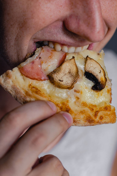 Primer plano retrato de emocionado joven hambriento feliz comiendo un pedazo de pizza, pizza de enfoque. Joven caucásico comiendo pizza
 - Foto, Imagen