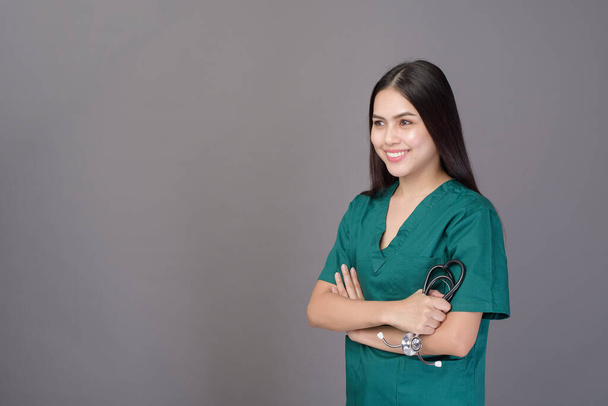 a female doctor wearing a green scrubs and stethoscope is on grey background studio - Фото, изображение