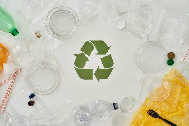 Flatlay composition with different empty plastic bottles, containers and recycling sign made of paper in the center over white background - Fotoğraf, Görsel