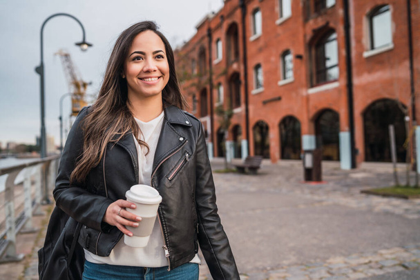 Portrait of beautiful young woman holding a cup of coffee outdoors. Urban concept. - Foto, afbeelding
