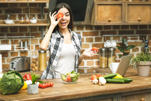 Laptop on kitchen table and cooking beautiful smiling girl. Food blogger concept. Relaxing - Photo, Image