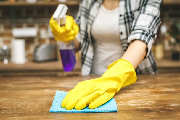 Vrouw in de keuken veegt stof af met een spray en een stofdoek tijdens het schoonmaken van haar huis, close-up - Foto, afbeelding