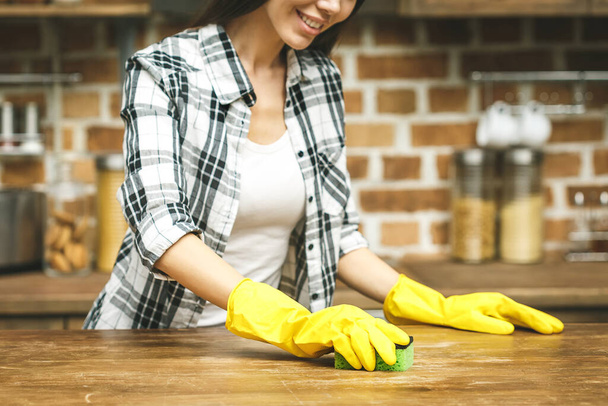Mulher na cozinha está sorrindo e limpando poeira usando um spray e um espanador enquanto limpa sua casa, close-up - Foto, Imagem