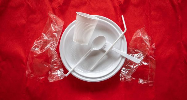 Some pieces of a disposable white plastic crockery over red background - Фото, изображение