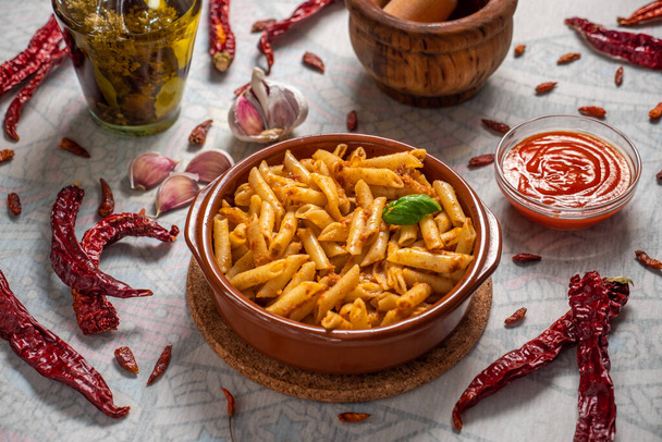 Macaroni with red pesto in a clay pan and some ingredients around - Photo, Image