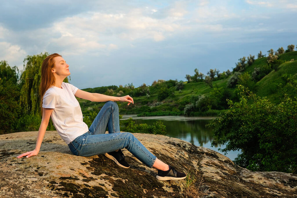 Relaxation, meditation mental health concept. National Relaxation Day. Red-haired woman meditates and relaxes in nature outdoor rocks - Photo, Image