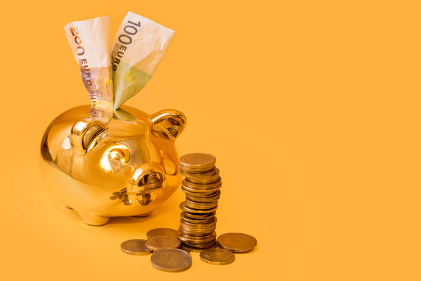 黄色の背景にお金の塔とユーロ紙幣と黄金の貯金箱。黄金のマネーボックスの近くにユーロコインのスタック。お金豚、お金の節約、お金箱、金融と投資の概念 - 写真・画像