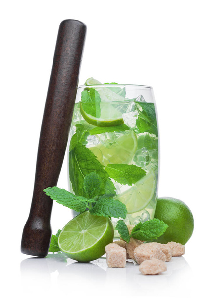 Glass of Mojito summer cocktail with ice cubes mint and lime on white background with cane sugar and raw lime with wooden muddler - Foto, Bild