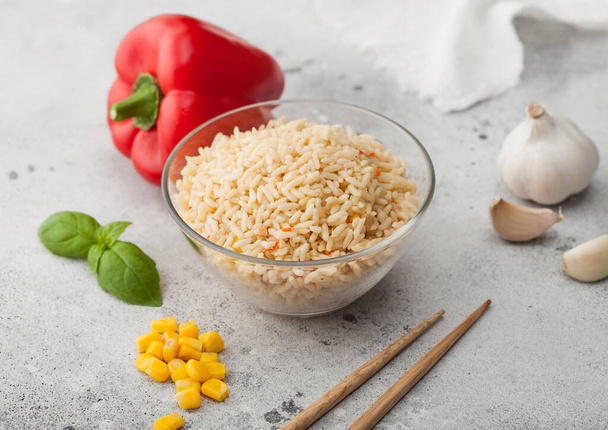 Glass bowl of boiled long grain basmati vegetable rice on light table background with sticks and red paprika with corn, garlic and basil. Macro - Fotografie, Obrázek