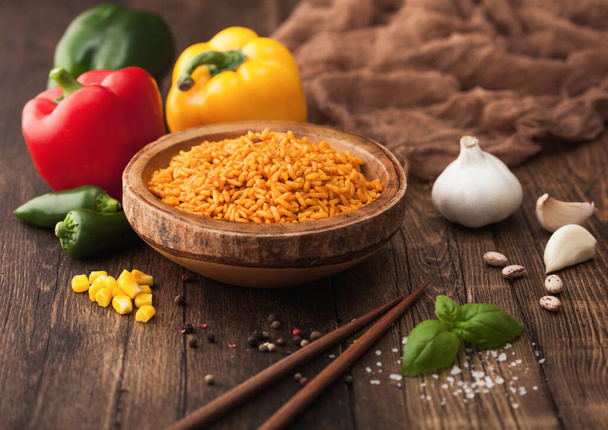 Wooden bowl with long grain basmati vegetable rice on wooden background with sticks and paprika pepper with corn,garlic and basil. - Foto, Imagen