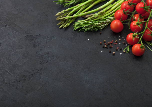 Black food background with asparagus, cherry tomatoes and rosemary on black table background with black pepper. Space for text - Zdjęcie, obraz