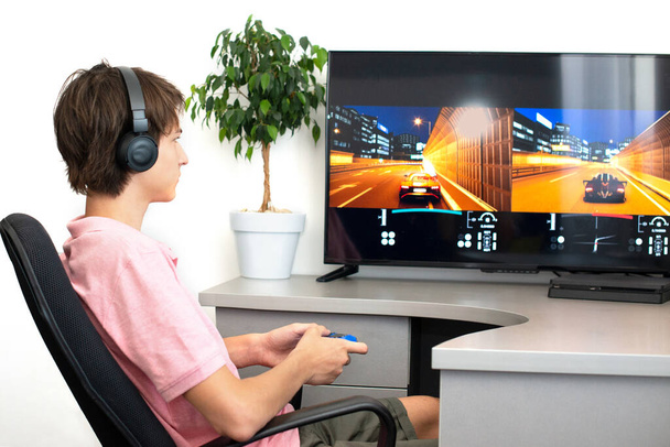 Хлопчик-підліток онлайн грає в комп'ютерну гру з навушниками та джойстиком, ігровою консоллю
. - Фото, зображення