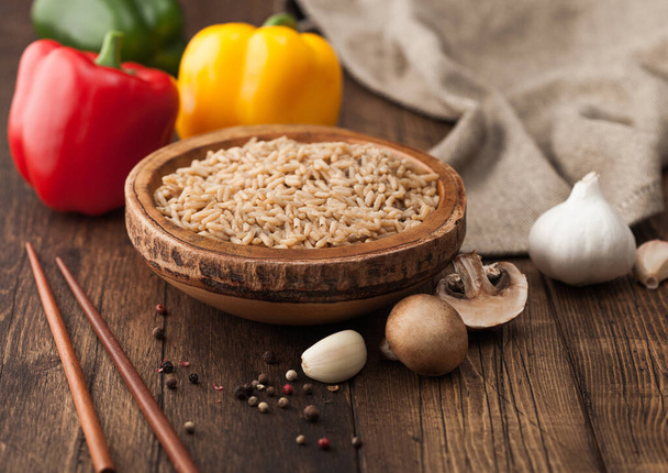 Wooden bowl with boiled long grain risotto rice with mushrooms on wooden background with sticks and linen kitchen towel and paprika pepper with garlic. - Photo, Image