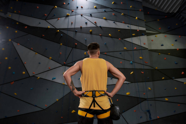 Fight Gravity. Young sportive man, rock climber with a bag of magnesia, chalk looking at artificial climbing wall. Concept of sport life and rock climbing - Photo, Image