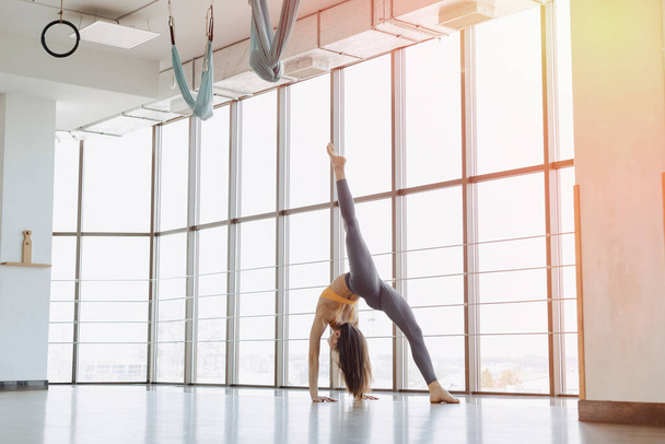 acogedora joven atractiva chica haciendo ejercicios de fitness con yoga en el suelo contra el fondo de ventanas panorámicas
 - Foto, imagen