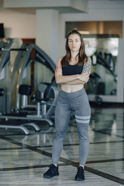 Attractive athletic girl stands on the background of simulators in the gym. healthy lifestyle and wellness. - Photo, image