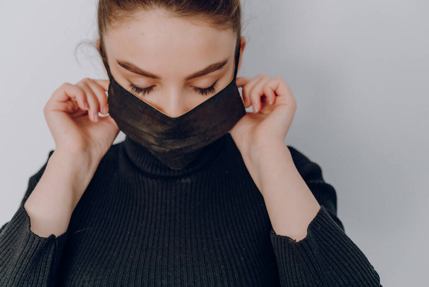 young cozy attractive girl on a light background wears a medical mask. use of personal protection. anti-epidemic and anti-pollution protection of the person. - Photo, Image