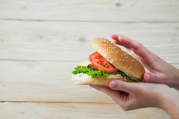 Hands holding homemade beef burger on wooden table. - Fotografie, Obrázek
