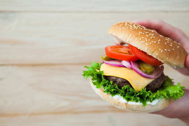 Mains tenant un hamburger de bœuf fait maison sur une table en bois. - Photo, image