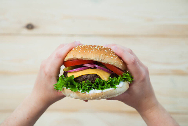 Mains tenant un hamburger de bœuf fait maison sur une table en bois. - Photo, image