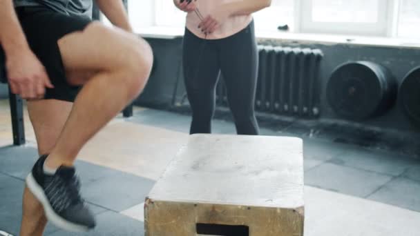 Low shot of anonymous man jumping on wooden box during crossfit workout in gym - Filmmaterial, Video