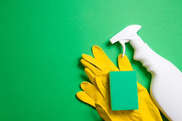 green sponges for cleaning, yellow rubber gloves and a white plastic spray bottle for detergent on a green background copy space top view - Foto, afbeelding