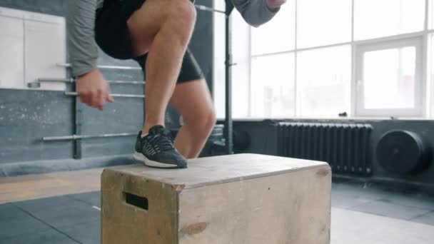 Slow motion of sportsman doing crossfit exercise box jump in modern gym - Video, Çekim