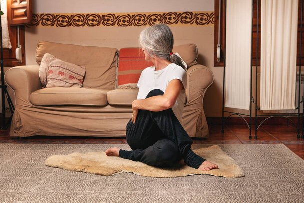 donna di mezza età con i capelli grigi praticare kundalini yoga nel suo soggiorno - Foto, immagini
