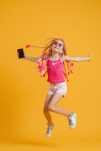 Beautiful European girl with dreadlocks jumping with mobile phone in the handand listen music on headphones - Foto, Imagem