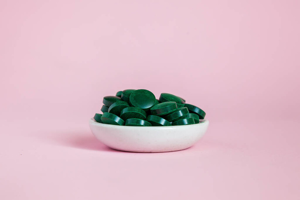 Close-up pile of green spirulina pills on a pink background. Super food concept. Spirulina dietary supplement - Photo, image