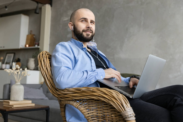 Brutální chlap sedí na židli a pracuje na laptopu. Koncept práce z domova - Fotografie, Obrázek