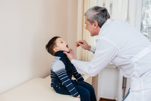A young boy is listened to and treated by an experienced doctor in a modern clinic. A virus, and an epidemic - Foto, Imagen