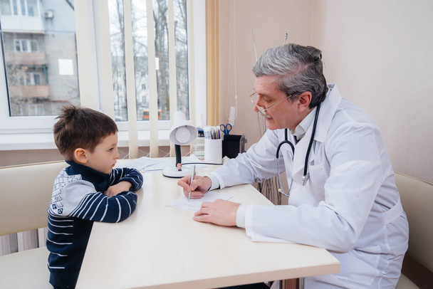 A young boy is listened to and treated by an experienced doctor in a modern clinic. A virus, and an epidemic - Foto, imagen