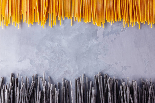 Black and yellow pasta on a gray background. Yellow and black spaghetti on cement background. Raw spaghetti bolognese. Food background concept. Top view - Fotoğraf, Görsel