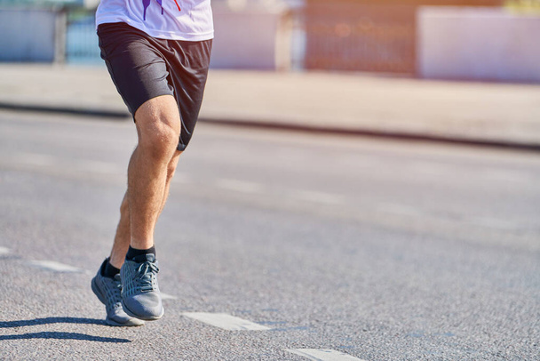 Бегущий человек. Атлетик бегает в спортивной одежде по городской дороге. Здоровый образ жизни, спортивное хобби. Уличные тренировки, бег на свежем воздухе - Фото, изображение