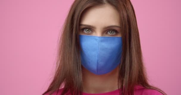 Close up of charming young lady taking off blue hygiene mask - Imágenes, Vídeo