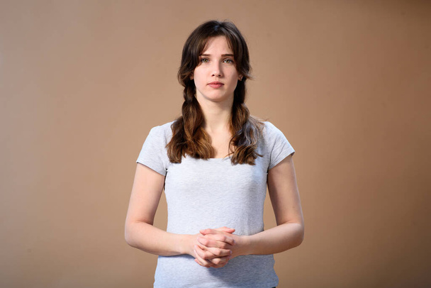 folded arms in front of a girl with pigtails on a beige background. girl listens attentively - Photo, Image