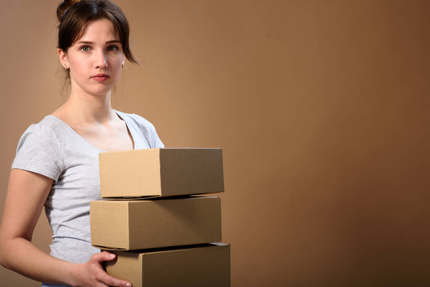 portrait of a cute girl with gathered hair with cardboard boxes in hands on a beige background. Mail delivery - Photo, Image