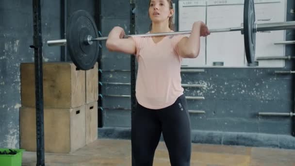 Muscular woman lifting barbell then squatting training legs working out in gym - Filmagem, Vídeo