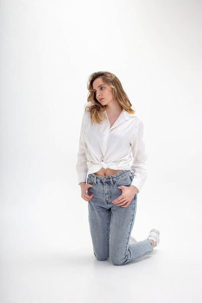 young cute pensive caucasian girl posing in white shirt, blue jeans at studio - Foto, Imagem