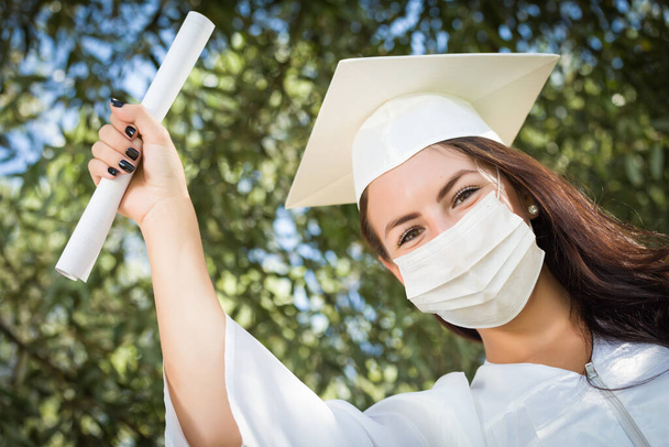 Absolwentka studiów w Cap and Sukienka nosząca medyczną maskę na twarz. - Zdjęcie, obraz
