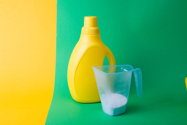 yellow plastic bottle with gel for washing children's clothes and a measuring cup with washing powder on a yellow-green background copy space - Fotoğraf, Görsel