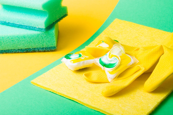 rubber gloves, capsules for dishwashers and sponges on a green and yellow background, places of copy top view, the choice between washing dishes with your hands or in the dishwasher - Φωτογραφία, εικόνα