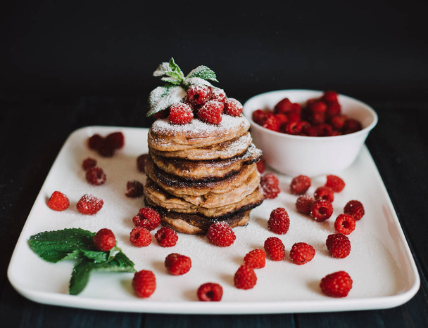 Chocolate pancakes with fresh raspberries and mint on black background - Photo, Image