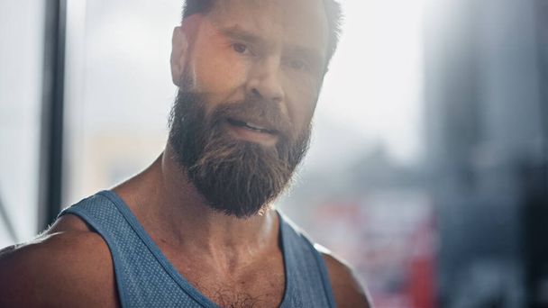 Portrait d'un athlète masculin barbu portant une chemise sans manches souriant à la caméra. Homme beau après l'exercice et l'entraînement Hardcore. L'homme obtient le travail fait - Photo, image