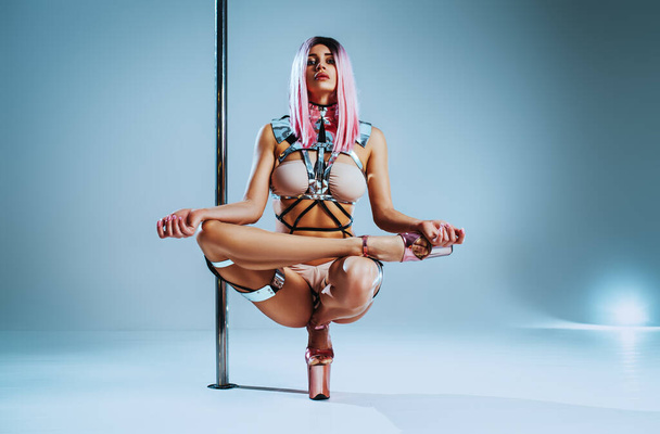 Young slim woman pole dancer sitting in yoga pose on white and blue background - Valokuva, kuva