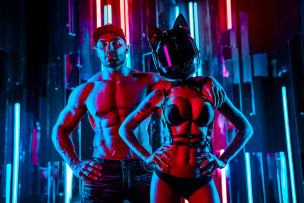 Strong man and woman posing in neon blue and red club lights. Tattoo on body. - Fotografie, Obrázek